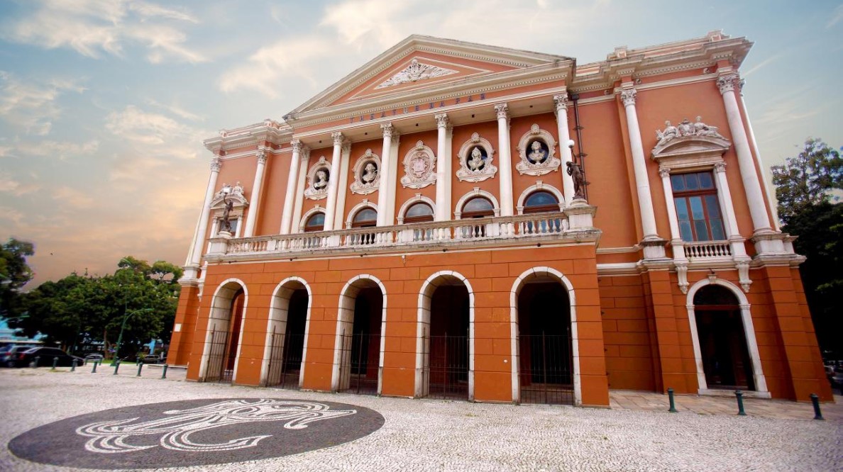 Fachada do Theatro da Paz em Belém, Pará, com sua arquitetura neoclássica, colunas imponentes e frontão decorado. No chão, em frente ao teatro, um mosaico em pedra portuguesa.